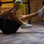 A man and woman perform core exercises with a medicine ball in a brick wall gym.